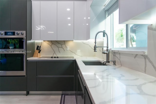 kitchen with stainless steel appliances, light wood-type flooring, white cabinetry, light stone countertops, and sink