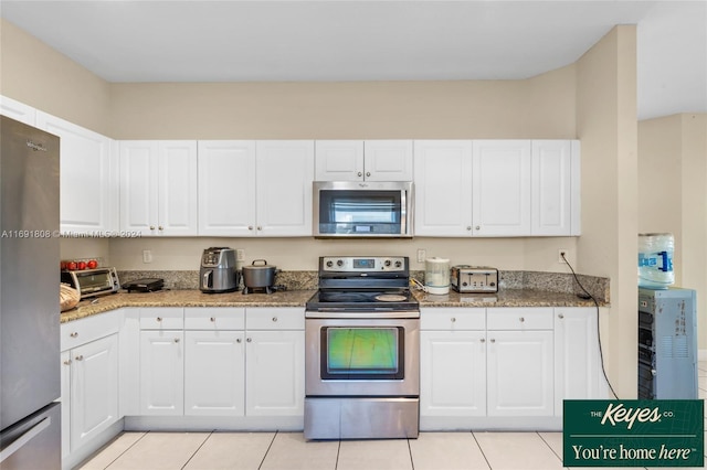 kitchen with white cabinets, light tile patterned floors, stainless steel appliances, and dark stone counters