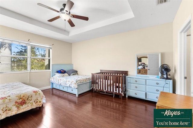 bedroom featuring a raised ceiling, ceiling fan, and dark hardwood / wood-style flooring