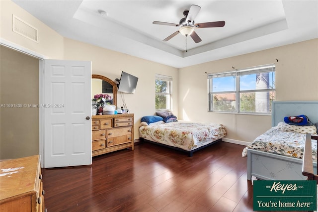 bedroom featuring ceiling fan, dark wood-type flooring, and a tray ceiling