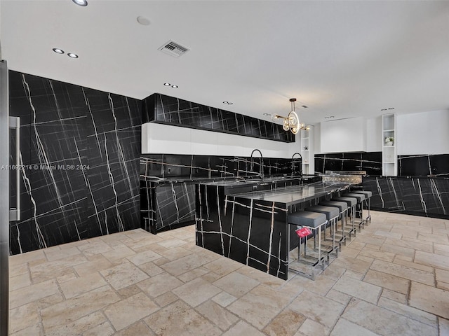 kitchen with decorative light fixtures, stone countertops, tile walls, a chandelier, and a breakfast bar area