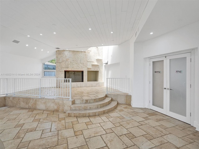 unfurnished living room with french doors, a large fireplace, and lofted ceiling