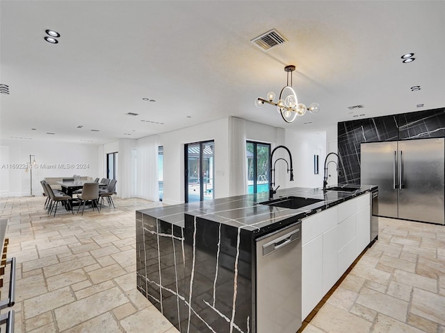 kitchen featuring sink, stainless steel appliances, decorative light fixtures, a kitchen island with sink, and white cabinets