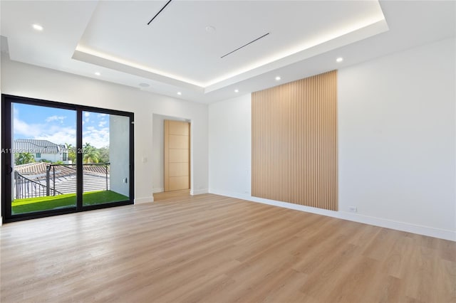 empty room with light wood-type flooring and a tray ceiling