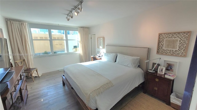 bedroom featuring baseboards, light wood-style floors, and rail lighting