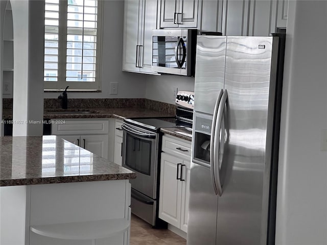 kitchen featuring dark stone counters, white cabinetry, appliances with stainless steel finishes, and sink