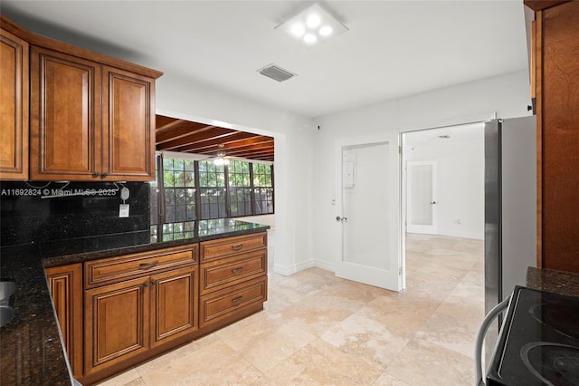 kitchen featuring brown cabinetry, tasteful backsplash, dark stone counters, and visible vents