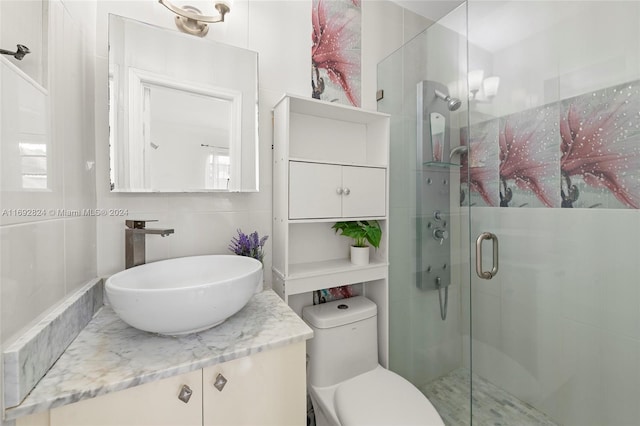 bathroom with walk in shower, vanity, tile walls, and toilet