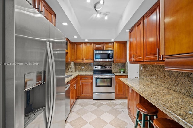 kitchen with a raised ceiling, light stone countertops, appliances with stainless steel finishes, and a kitchen breakfast bar