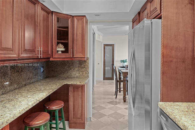 kitchen featuring stainless steel fridge, tasteful backsplash, light stone counters, and a breakfast bar area