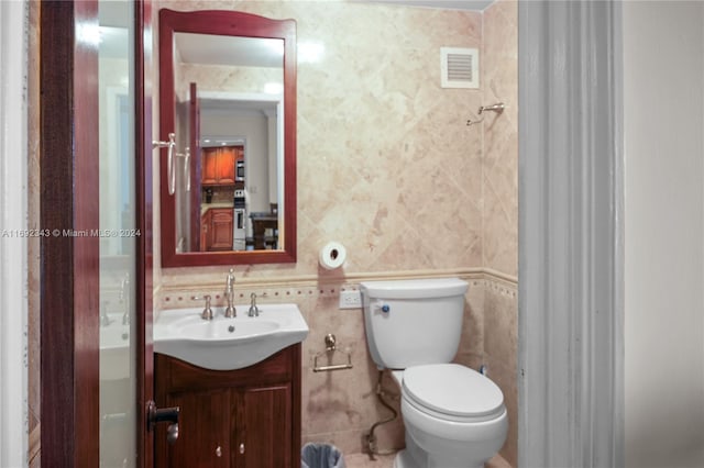 bathroom with vanity, toilet, and tile walls