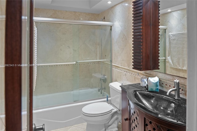 full bathroom with shower / bath combination with glass door, vanity, tile patterned floors, toilet, and tile walls