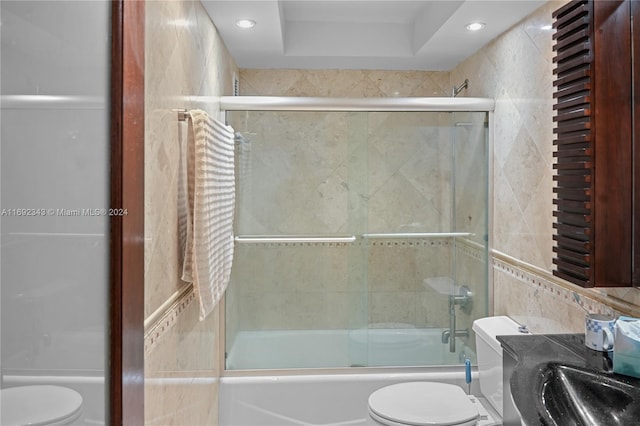 full bathroom featuring toilet, combined bath / shower with glass door, a tray ceiling, and sink