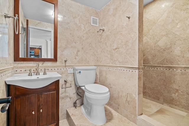 bathroom featuring tiled shower, vanity, toilet, and tile walls