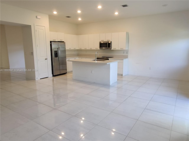 kitchen featuring white cabinetry, stainless steel appliances, light tile patterned floors, and an island with sink