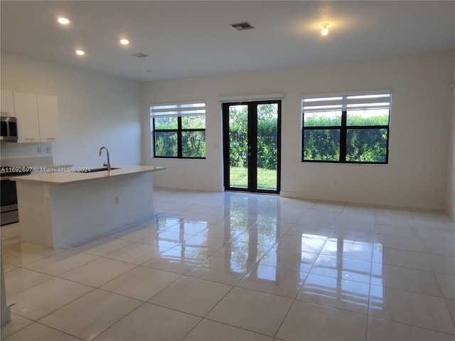 kitchen featuring stainless steel appliances, sink, light tile patterned floors, an island with sink, and white cabinets