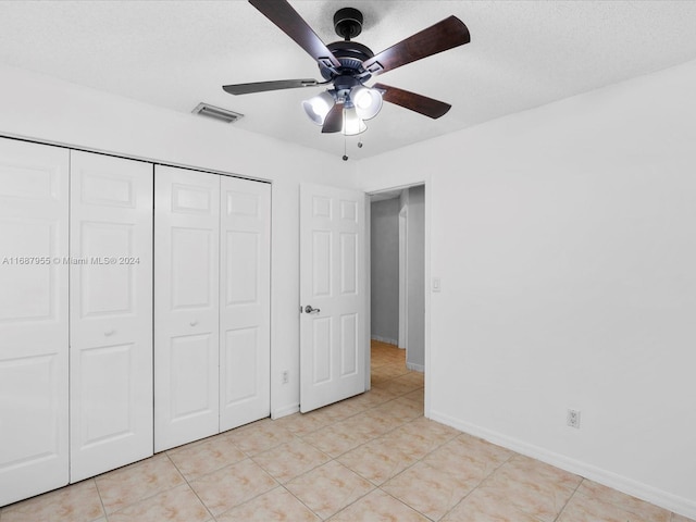 unfurnished bedroom featuring ceiling fan, light tile patterned floors, a textured ceiling, and a closet