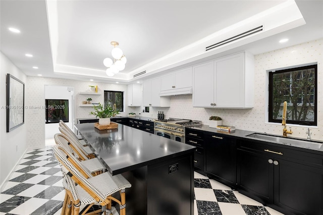 kitchen with a kitchen island, white cabinetry, sink, a breakfast bar, and a tray ceiling