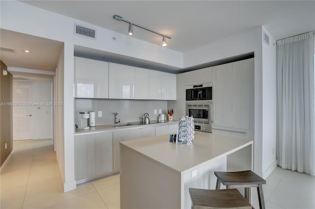 kitchen with light tile patterned flooring, sink, a breakfast bar, a center island, and white cabinets