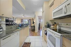 kitchen featuring dark stone counters, white appliances, and light tile patterned flooring