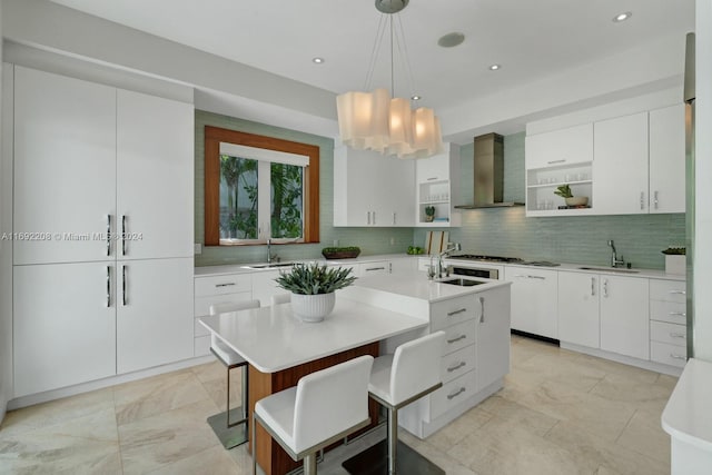 kitchen featuring white cabinets, a center island with sink, wall chimney exhaust hood, and sink