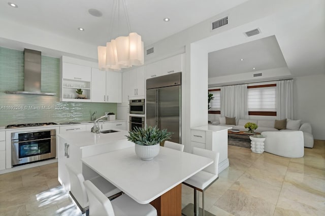 kitchen with a kitchen island with sink, wall chimney range hood, a breakfast bar area, and appliances with stainless steel finishes