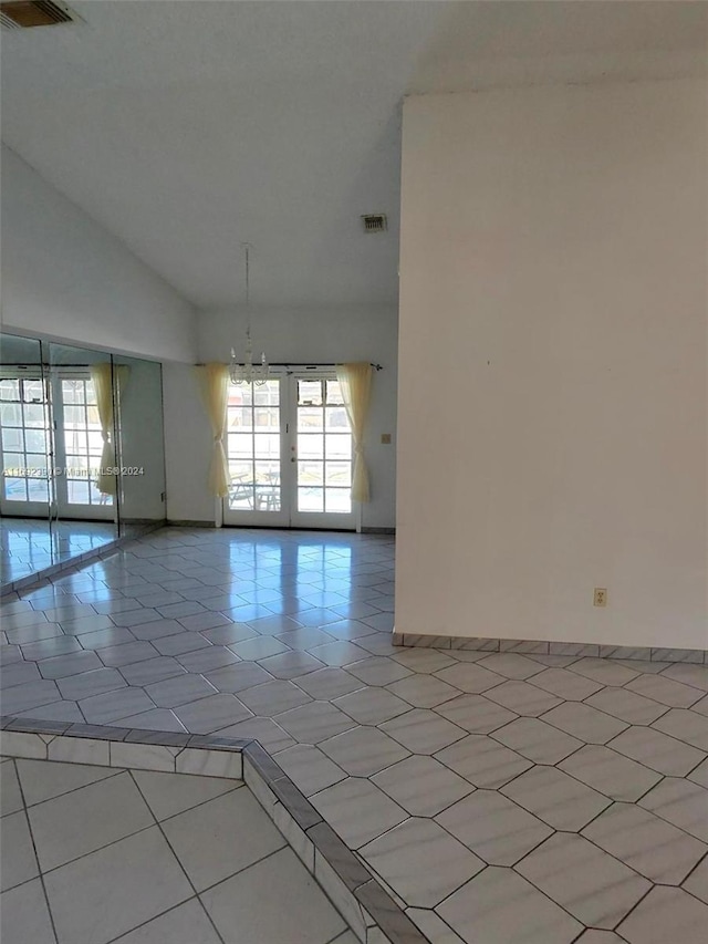 tiled empty room featuring vaulted ceiling and french doors