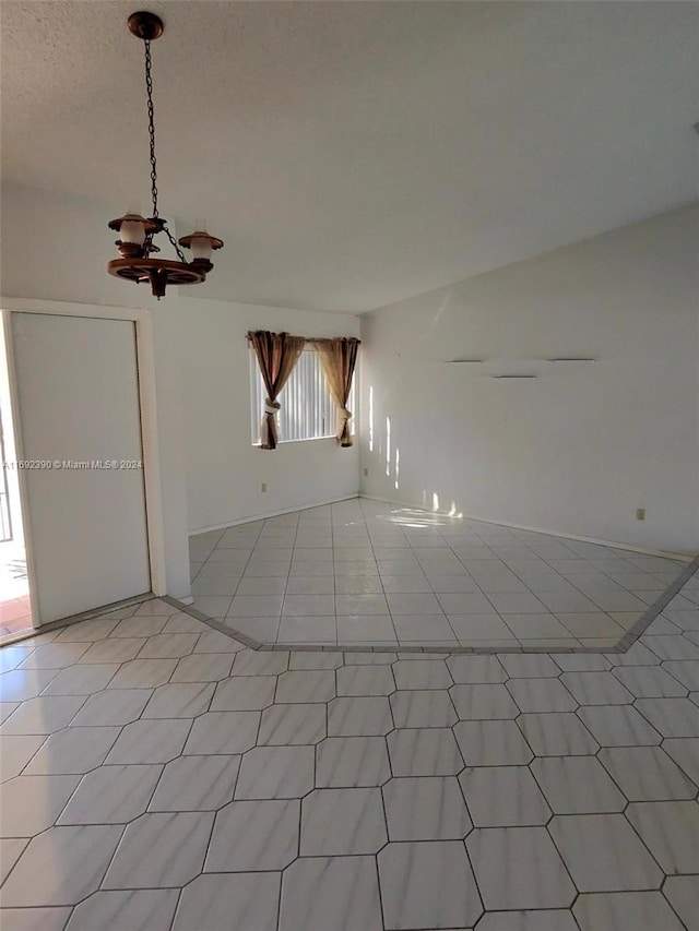 tiled empty room featuring a textured ceiling and a notable chandelier