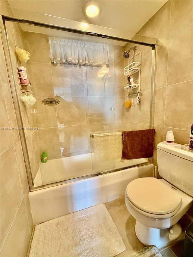 bathroom with shower / bath combination with glass door, tile patterned floors, toilet, and tile walls