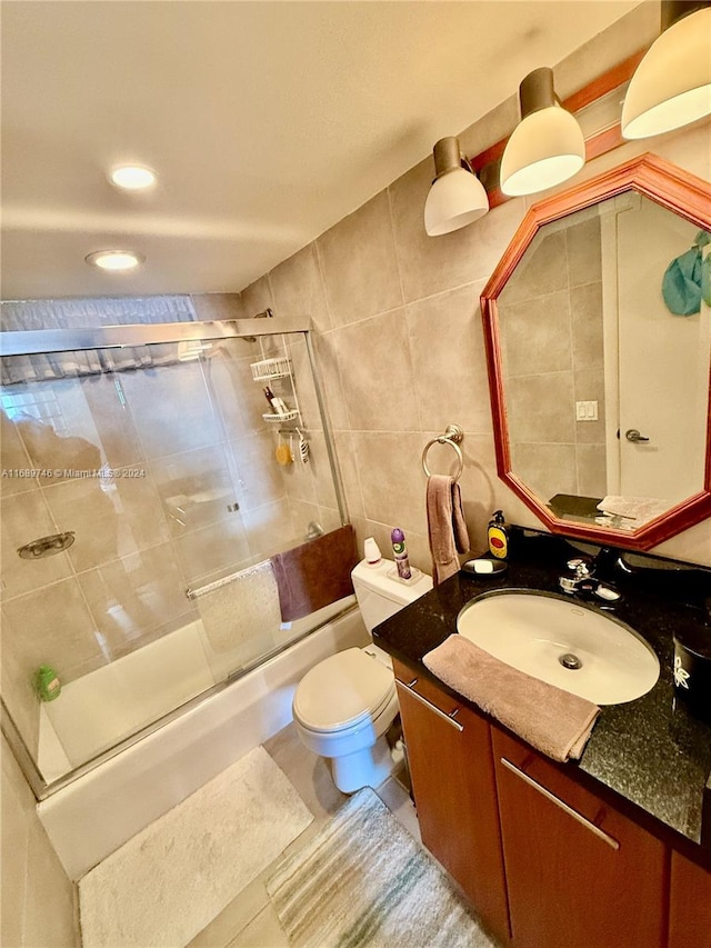 full bathroom featuring vanity, bath / shower combo with glass door, tile patterned floors, toilet, and tile walls