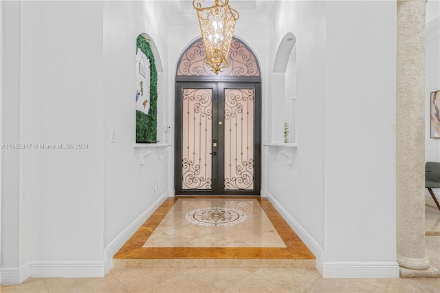 foyer with an inviting chandelier, tile patterned flooring, ornamental molding, and french doors