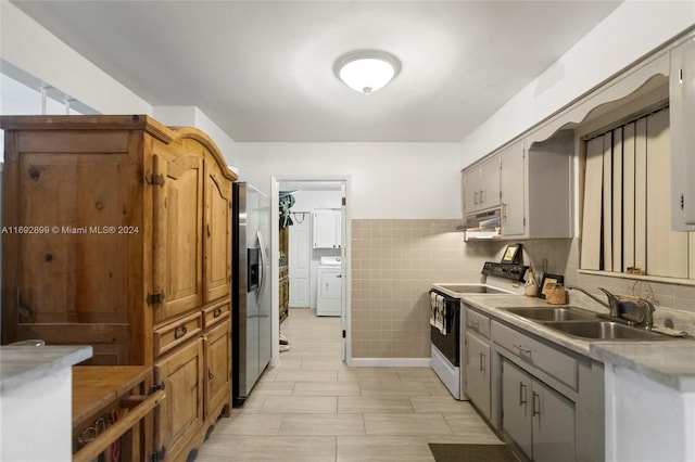 kitchen with sink, white electric stove, tile walls, washer / dryer, and stainless steel fridge with ice dispenser