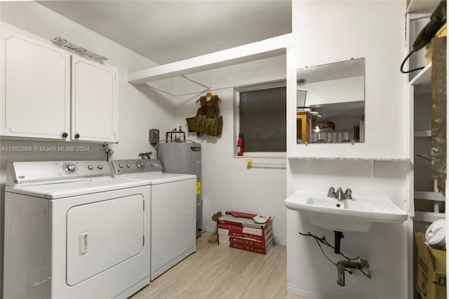 clothes washing area with washer and dryer, electric water heater, light hardwood / wood-style floors, and cabinets