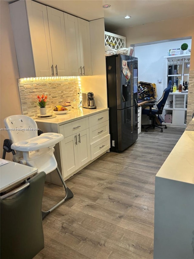 kitchen with white cabinets, light hardwood / wood-style floors, tasteful backsplash, and black refrigerator