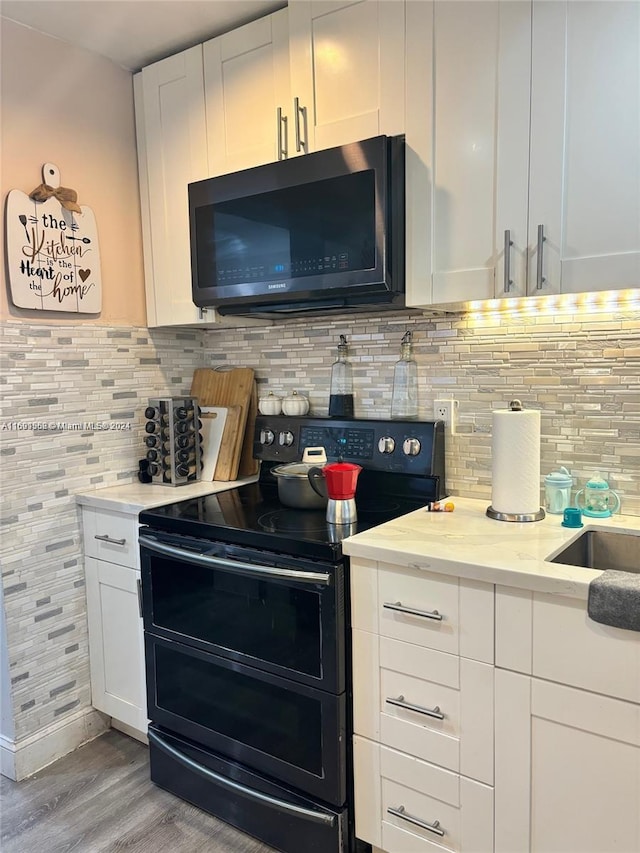 kitchen with light stone counters, stainless steel appliances, backsplash, white cabinets, and light hardwood / wood-style flooring