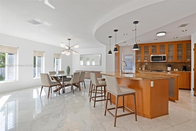 kitchen featuring tasteful backsplash, light stone counters, a center island with sink, pendant lighting, and sink