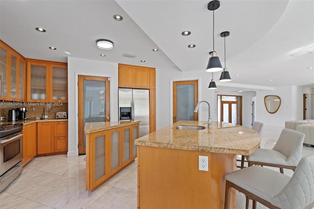 kitchen with backsplash, appliances with stainless steel finishes, decorative light fixtures, sink, and a kitchen island with sink