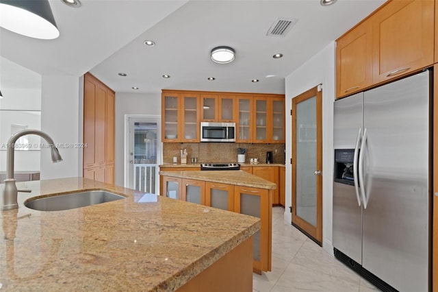 kitchen with light stone counters, stainless steel appliances, backsplash, sink, and an island with sink