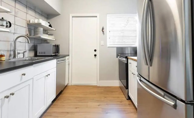 kitchen with stainless steel appliances, sink, tasteful backsplash, white cabinetry, and light hardwood / wood-style flooring