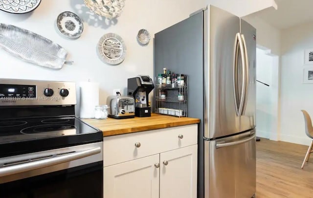 kitchen with butcher block countertops, white cabinetry, light hardwood / wood-style floors, and stainless steel appliances