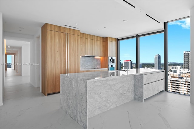 kitchen featuring light stone countertops, stainless steel double oven, expansive windows, and a spacious island