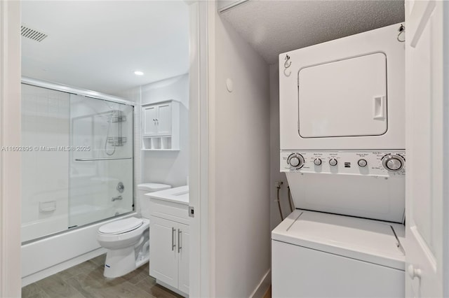 clothes washing area with hardwood / wood-style floors, a textured ceiling, and stacked washing maching and dryer