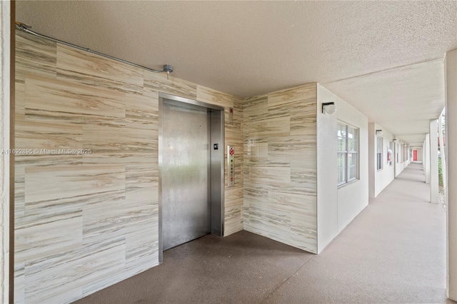 hallway with a textured ceiling, elevator, and concrete floors