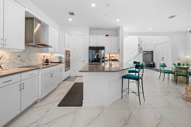 kitchen featuring white cabinets, black electric stovetop, wall chimney range hood, and an island with sink