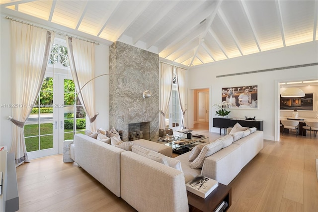 living room with french doors, high vaulted ceiling, a premium fireplace, and light wood-type flooring