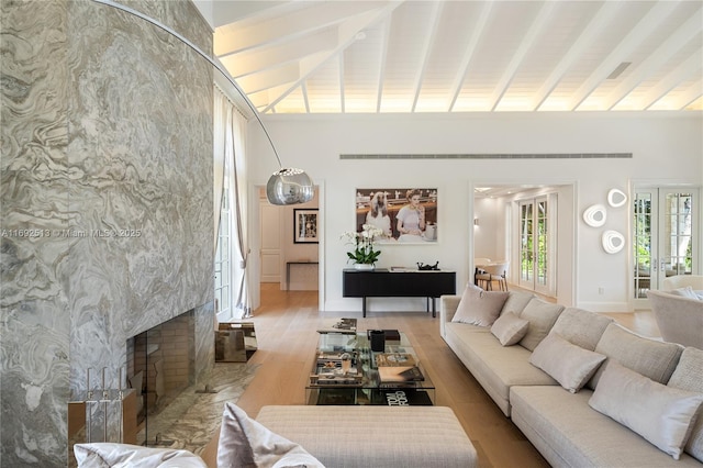 living room featuring beam ceiling, high vaulted ceiling, a high end fireplace, french doors, and light wood-type flooring