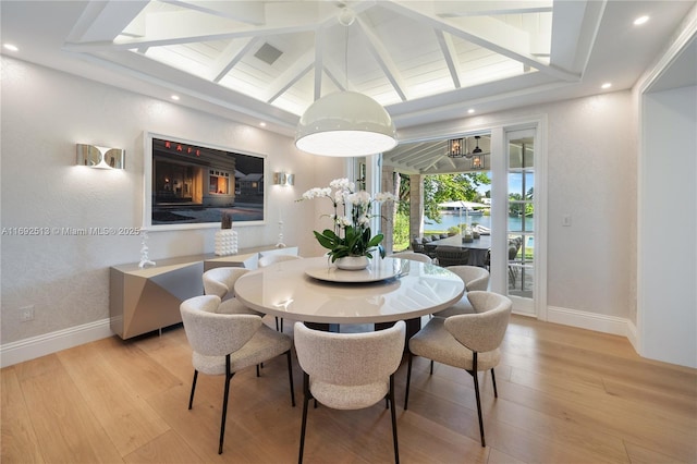 dining space featuring lofted ceiling with beams, a water view, and light wood-type flooring