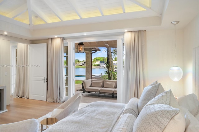 bedroom with access to outside, light hardwood / wood-style floors, lofted ceiling with beams, and a water view