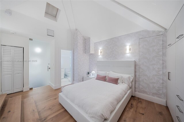 bedroom with high vaulted ceiling, light hardwood / wood-style floors, and ensuite bath