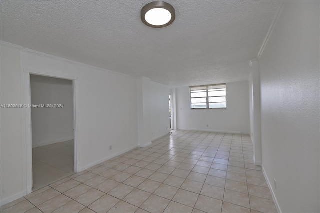 empty room with a textured ceiling, light tile patterned floors, and crown molding